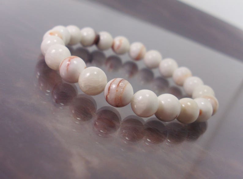 K&ouml;nnte beinhalten: Armband aus wei&szlig;en und rot gestreiften Edelsteinen. Das Armband besteht aus runden Perlen.