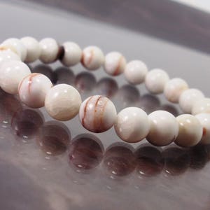 K&ouml;nnte beinhalten: Ein wei&szlig;es Armband mit braunen Streifen aus runden Perlen.