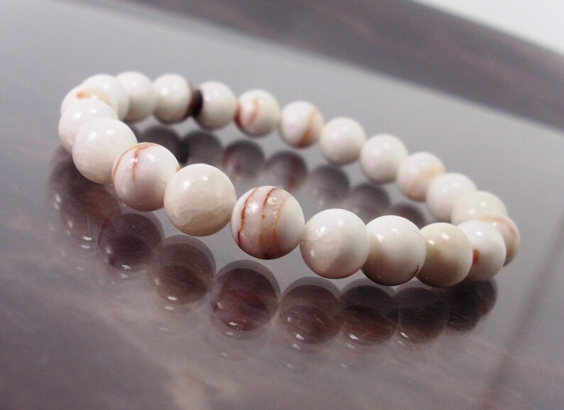 K&ouml;nnte beinhalten: Ein wei&szlig;es Armband mit braunen Streifen aus runden Perlen.