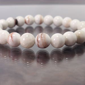 K&ouml;nnte beinhalten: Ein wei&szlig;es Armband mit braunen Streifen aus runden Perlen.