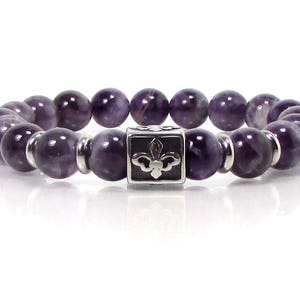 May include: A purple amethyst gemstone bracelet with a silver charm featuring a fleur-de-lis design.