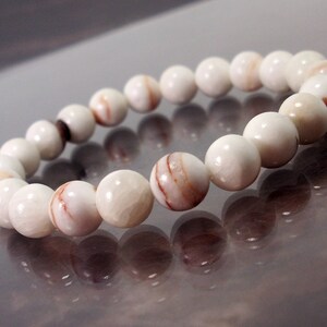 K&ouml;nnte beinhalten: Armband aus wei&szlig;en Muschelperlen mit braunen und wei&szlig;en Marmorierungen. Die Perlen sind rund und glatt.