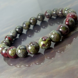 Könnte beinhalten: Ein Armband aus grün, rot und braun gesprenkeltem Stein mit runden Perlen.