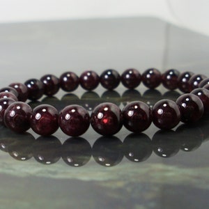 May include: A dark red gemstone bracelet with round beads. The bracelet is made of natural stones and is approximately 7 inches in length.