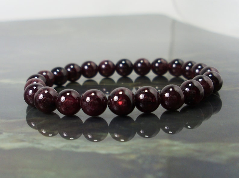 May include: A dark red gemstone bracelet with round beads. The bracelet is made of natural stones and is approximately 7 inches in length.
