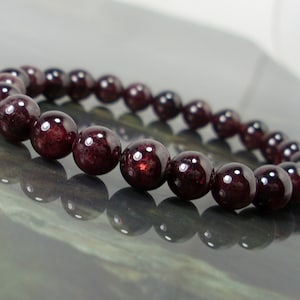 May include: A red gemstone bracelet made with round beads. The bracelet is made with dark red garnet beads.