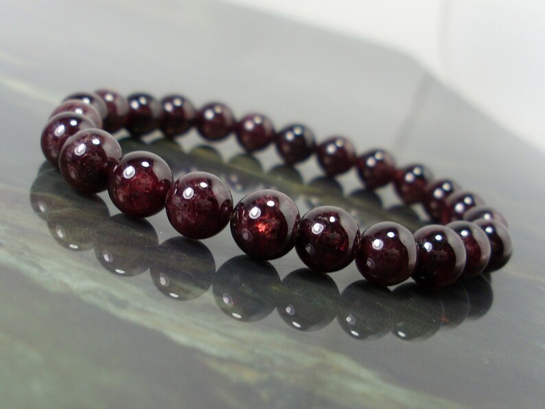 May include: A red gemstone bracelet made with round beads. The bracelet is made with dark red garnet beads.