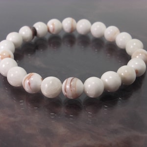 K&ouml;nnte beinhalten: Ein wei&szlig;es Armband aus runden Perlen mit braunen Wirbeln. Das Armband ist aus nat&uuml;rlichen Materialien.