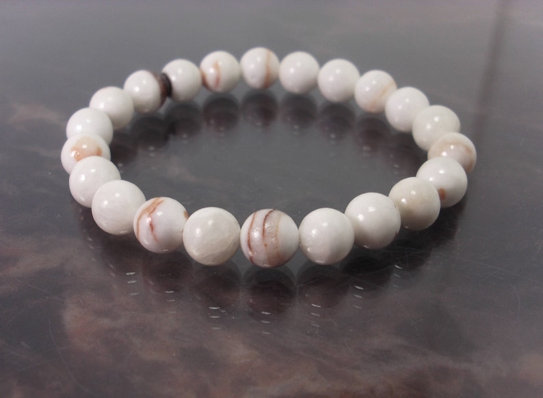 K&ouml;nnte beinhalten: Ein wei&szlig;es Armband aus runden Perlen mit braunen Wirbeln. Das Armband ist aus nat&uuml;rlichen Materialien.