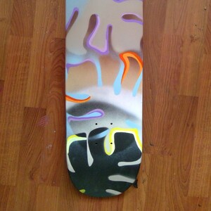 May include: A skateboard deck with a colorful abstract design featuring blue, orange, purple, and yellow paint splatters. The deck is made of wood and has a black grip tape.