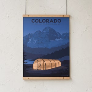 May include: A poster print featuring a nighttime landscape of Colorado with mountains, trees, and a greenhouse. The word "COLORADO" is at the top, with the text "ENLIGHTENING THE NATION ON LEGALIZATION" below it. The poster is held by wooden bars.
