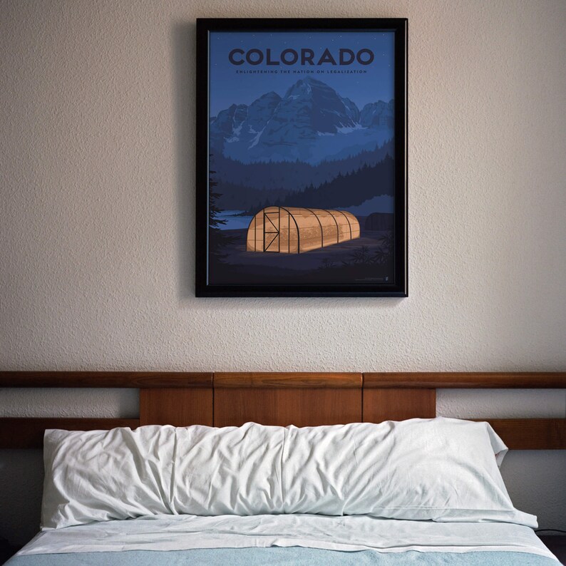 May include: Framed poster featuring a Colorado landscape with mountains, trees, and a glowing greenhouse. The poster has the word "COLORADO" at the top. The poster is hanging above a bed with a white pillow and blue sheet.