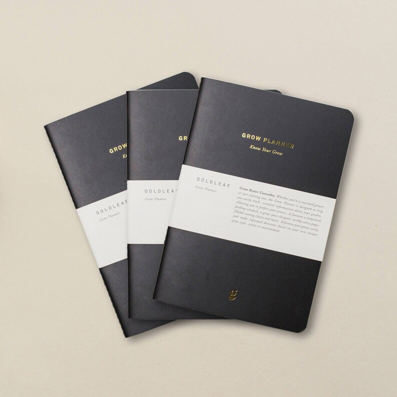 May include: Three black Grow Planner notebooks with gold lettering. The front cover of the notebook on the right has the text "GROW PLANNER Know Your Grow" and "GOLDLEAF Grow Planner" printed on a white label. The text on the label reads "Grow Better Cannabis. Whether you're a seasoned grower or just starting out, the Grow Planner is designed to help you manage every aspect of your cultivation. It's a fully customizable daily track for your plants, from seed to harvest, allowing you to perfectly document your grow process. Includes daily notes, plant measurements, nutrient records, flushing schedule, a grow journal, and a customizable grid to make charts and diagrams.  Hand-drawn pages and high-quality, environmentally friendly paper.