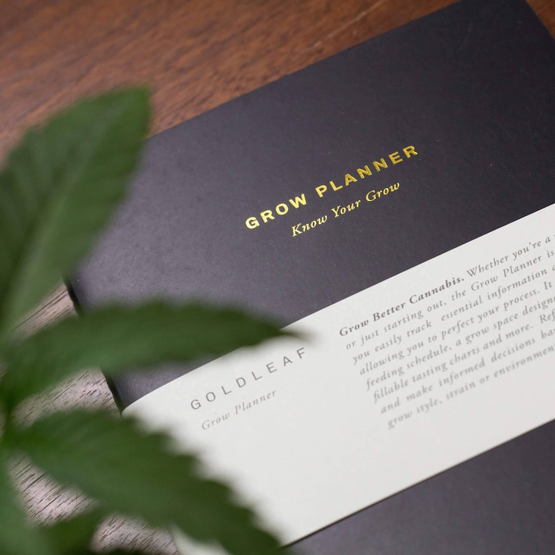 May include: A black grow planner with gold lettering that reads "Grow Planner Know Your Grow" and "Goldleaf Grow Planner". The planner has a white label with text that reads "Grow Better Cannabis. Whether you're a...", describing the planner's purpose.