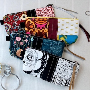Puede incluir: Cuatro estuches rectangulares con cremallera que presentan varios patrones de tela, incluyendo cachemir rojo, coronas doradas sobre blanco, estampados botánicos florales y diseños florales en blanco y negro con detalles en tela negra.