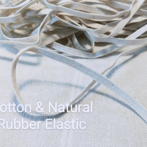 May include: A coil of off-white, flat elastic cord featuring a woven texture with small dark flecks throughout. The text Cotton & Natural Rubber Elastic is printed in white over the lower portion of the image, describing the material composition.