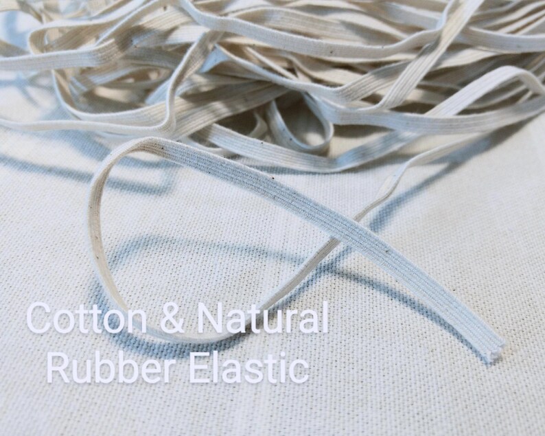 May include: A coil of off-white, flat elastic cord featuring a woven texture with small dark flecks throughout. The text Cotton & Natural Rubber Elastic is printed in white over the lower portion of the image, describing the material composition.