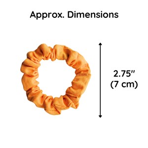 May include: A bright orange fabric scrunchie with a gathered, ruffled texture. The text 'Approx. Dimensions' appears above the object, and a vertical arrow indicates a measurement of 2.75 inches, which is equivalent to 7 cm in total diameter.