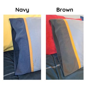 May include: Two rectangular pillowcases are displayed side-by-side. The left pillowcase is navy blue with a light blue panel and a thin orange stripe. The right pillowcase is brown with a light blue panel and a thin orange stripe. Text reads Navy and Brown.