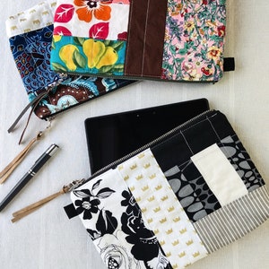 Peut inclure: Une pochette en tissu patchwork noir et blanc avec une fermeture à glissière. La pochette est faite de différents tissus, dont un motif géométrique noir et blanc, un tissu blanc avec des couronnes dorées et un motif floral noir et blanc. La pochette est posée sur une table avec une tablette et un stylo.