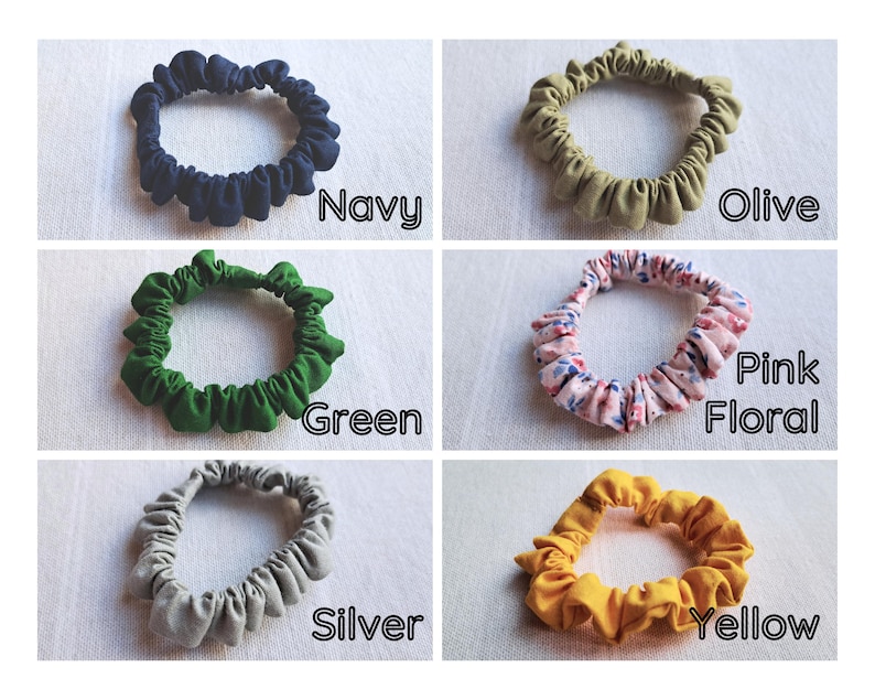 May include: A collection of six fabric hair scrunchies in various colors and patterns. The set includes solid navy, olive, green, silver, and yellow scrunchies, along with one pink floral patterned scrunchie. Each item is labeled with its color name.