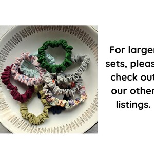 May include: A collection of fabric hair scrunchies in various colors including green, maroon, olive, grey, and floral patterns, arranged inside a white bowl with a leaf pattern. The text reads: For larger sets, please check out our other listings.