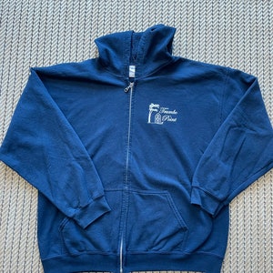 May include: Navy blue zip-up hoodie with a front pocket and a hood. The hoodie features a white graphic of a palm tree and the text "Trumbo Point". The zipper is silver.