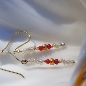 May include: Gold earrings with pink and white beads. The earrings are made with small, irregular shaped white beads and two pink beads with gold accents.