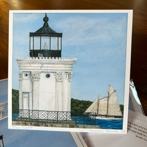 May include: A square print of a lighthouse and sailboat on the water under a blue sky. The lighthouse is white with a black top. The sailboat has white sails. The text "Bug Light" is visible.
