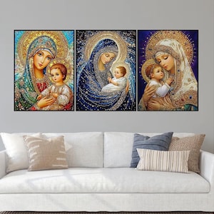 May include: Three framed religious art pieces depicting the Virgin Mary and baby Jesus. The artwork features detailed depictions with gold halos, intricate clothing, and a serene color palette of blues, greens, and golds. The art is displayed above a white sofa.