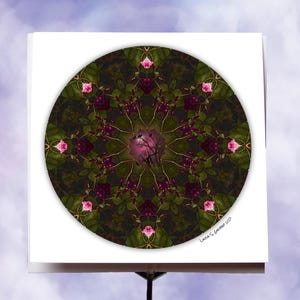 May include: A square white card featuring a circular floral design. The design is a kaleidoscope of dark green leaves, pink roses, and purple berries. The center has a pink hue with a tree silhouette. The artist's signature is in the bottom right corner.