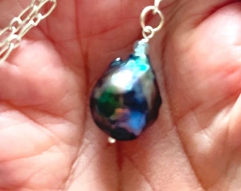 May include: A silver chain necklace with a large, iridescent black pearl pendant.