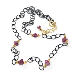 Könnte beinhalten: Eine schwarze Kettenkette mit goldenen Akzenten und rosafarbenen Edelsteinperlen. Die Kette hat einen Karabinerverschluss.