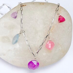May include: A silver chain necklace with five dangling gemstone charms. The charms are in shades of pink, purple, and blue.