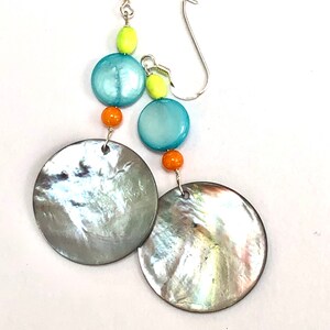 Può includere: Un paio di orecchini pendenti in argento con perline turchesi, arancioni e verde lime e grandi dischi di conchiglia grigia iridescente.
