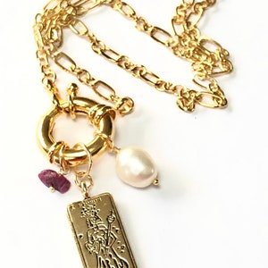 May include: Gold chain necklace with a large gold ring clasp, a small gold charm with a tarot card image, a white pearl, and a small red gemstone.
