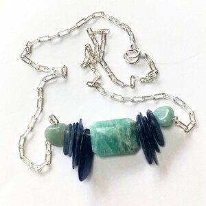 May include: A silver chain necklace with a pendant made of blue and green stones. The pendant is made of several different shapes and sizes of stones, including a large rectangular green stone.