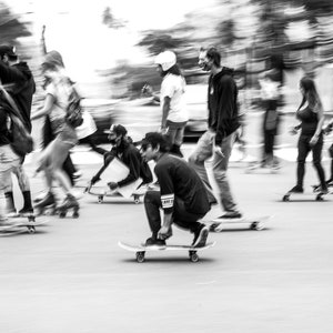 Puede incluir: Un grupo de personas patinando en patineta por una calle. Las personas están borrosas en movimiento, creando una sensación de velocidad y energía. La imagen está en blanco y negro.