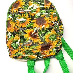 May include: A clear plastic backpack with green straps. The backpack has a sunflower and bird print.