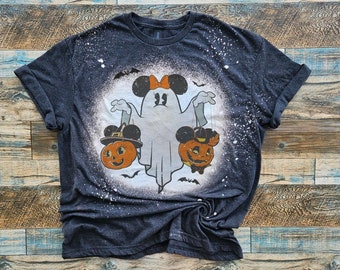 Może przedstawiać: Czarny T-shirt z wzorem rozpryskanym wybielaczem, przedstawiającym ducha z uszami Myszki Miki i kokardką, trzymającego dwie dynie z uszami Myszki Miki i kapeluszami. Dynie mają pomarańczowe twarze i czarne oczy.