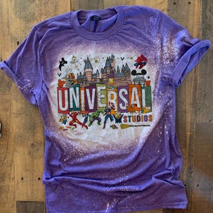 May include: Purple t-shirt with a bleached design featuring the Universal Studios logo and various cartoon characters, including Spiderman, Harry Potter, and the Minions.