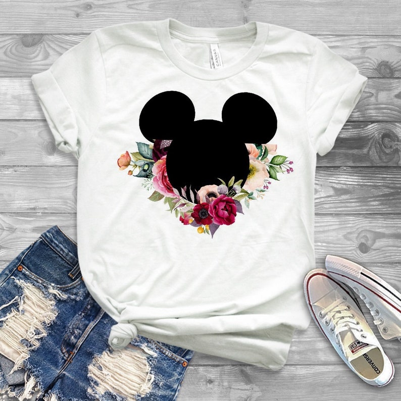 May include: White t-shirt with a black silhouette of Mickey Mouse's head surrounded by a floral wreath with pink, red, and white flowers.