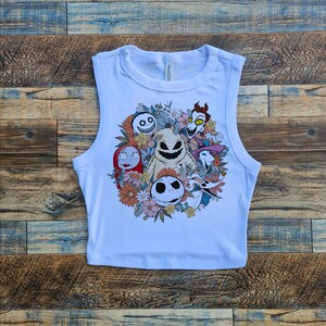 May include: White sleeveless crop top with a colorful graphic print of characters from the Nightmare Before Christmas movie. The characters are surrounded by flowers.