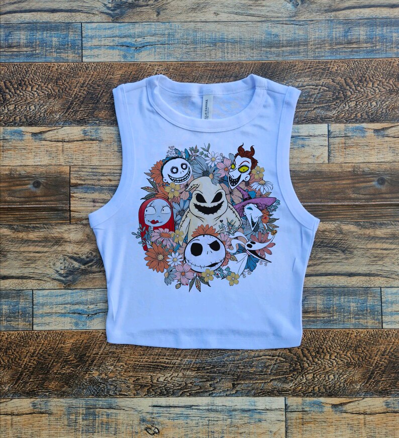 May include: White sleeveless crop top with a colorful graphic print of characters from the Nightmare Before Christmas movie. The characters are surrounded by flowers.