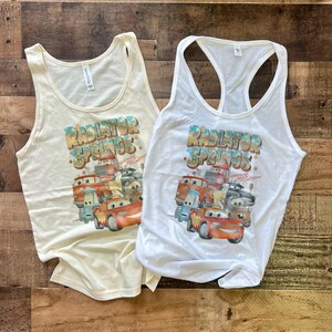 May include: Two white tank tops with a graphic print of cars from the movie Cars. The text "Radiator Springs" is printed on the front of the shirts.
