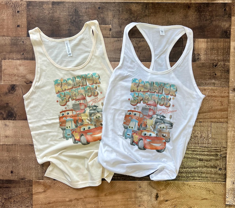 May include: Two white tank tops with a graphic print of cars from the movie Cars. The text "Radiator Springs" is printed on the front of the shirts.