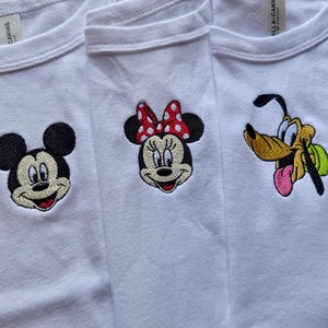 May include: Three white t-shirts with embroidered cartoon character faces. Mickey Mouse, Minnie Mouse with a red polka dot bow, and Pluto are featured. The shirts are made of a soft material.