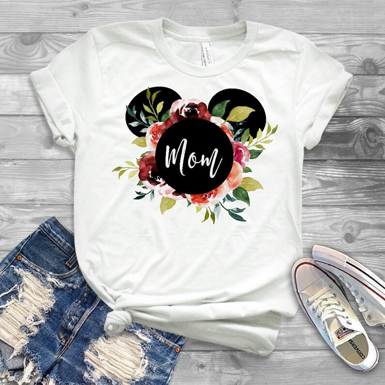 May include: White t-shirt with a black Mickey Mouse head silhouette with red, pink, and green floral accents. The word "Mom" is written in a black circle in the center of the silhouette.