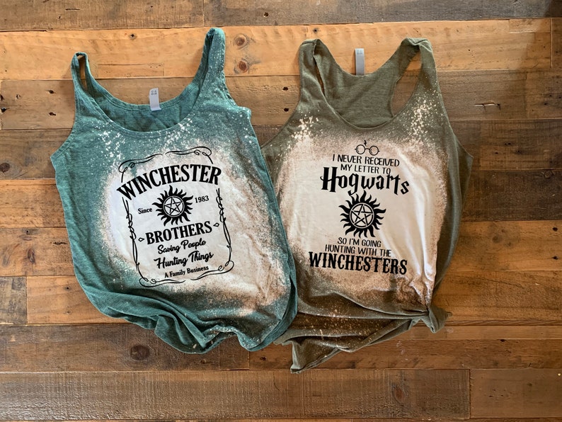 K&ouml;nnte beinhalten: Zwei gr&uuml;ne Tanktops mit Bleiche-Spritzer-Designs. Das erste Tanktop hat eine schwarz-wei&szlig;e Grafik mit dem Text "Winchester" und "Brothers" mit einem Symbol. Das zweite Tanktop hat eine schwarz-wei&szlig;e Grafik mit dem Text "Ich habe meinen Brief nach Hogwarts nie erhalten" und "Also gehe ich mit den Winchesters auf die Jagd" mit einem Symbol.