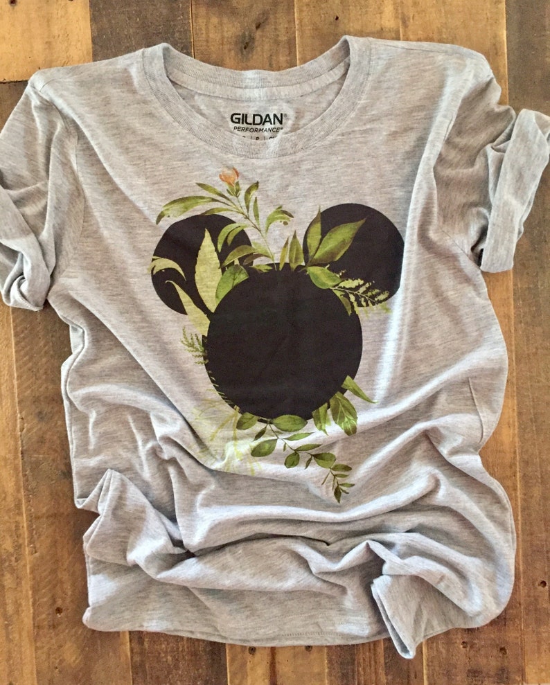 May include: Gray t-shirt with a black Mickey Mouse head silhouette surrounded by green leaves and flowers. The shirt has the Gildan Performance logo on the tag.